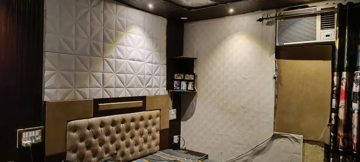A channel-tufted fabric headboard bed against a white 3D-textured geometric wall panel, under a dark wood slatted ceiling
