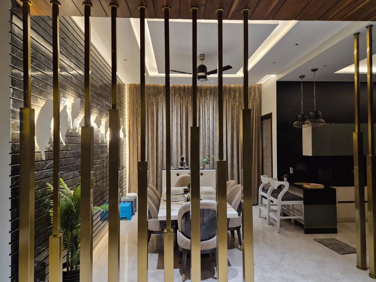 Dining table for six seen through a floor-to-ceiling brass vertical-rod screen, with a grooved dark-marble wall and wood-clad ceiling behind