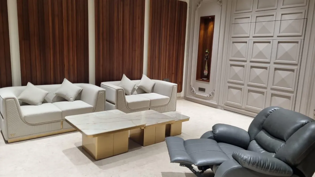 Living room with cream leather sofas trimmed in gold, a marble-and-brass coffee table, and a fluted walnut panelling wall beside a 3D geometric feature wall.