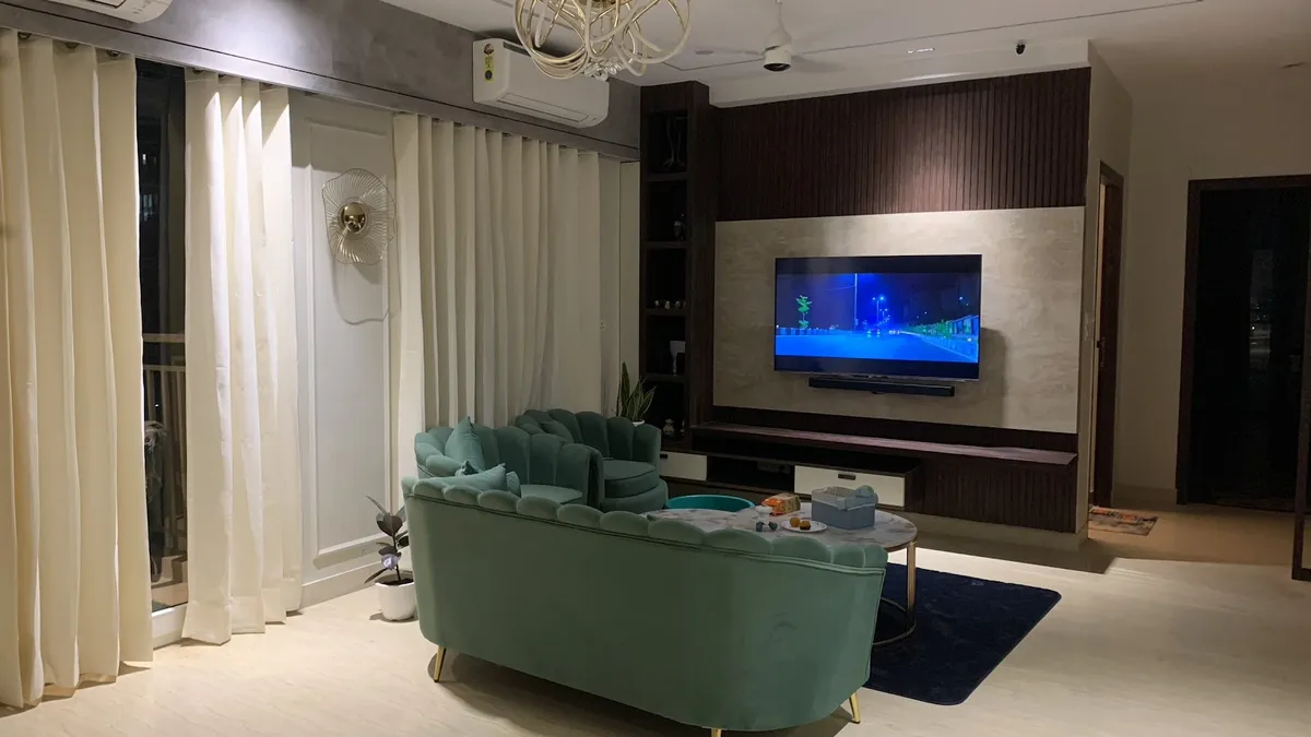 Living room with a mint-green scalloped velvet sofa, a stone-and-wood TV feature wall, a gold branch chandelier, and a round marble coffee table on a navy rug.