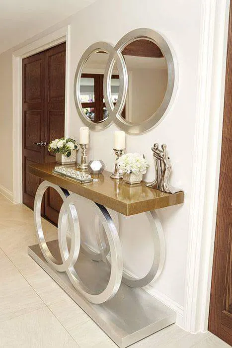 Entryway console table with an interlocking silver ring base and gold top, styled with candles, florals, and a pair of round mirrors above.