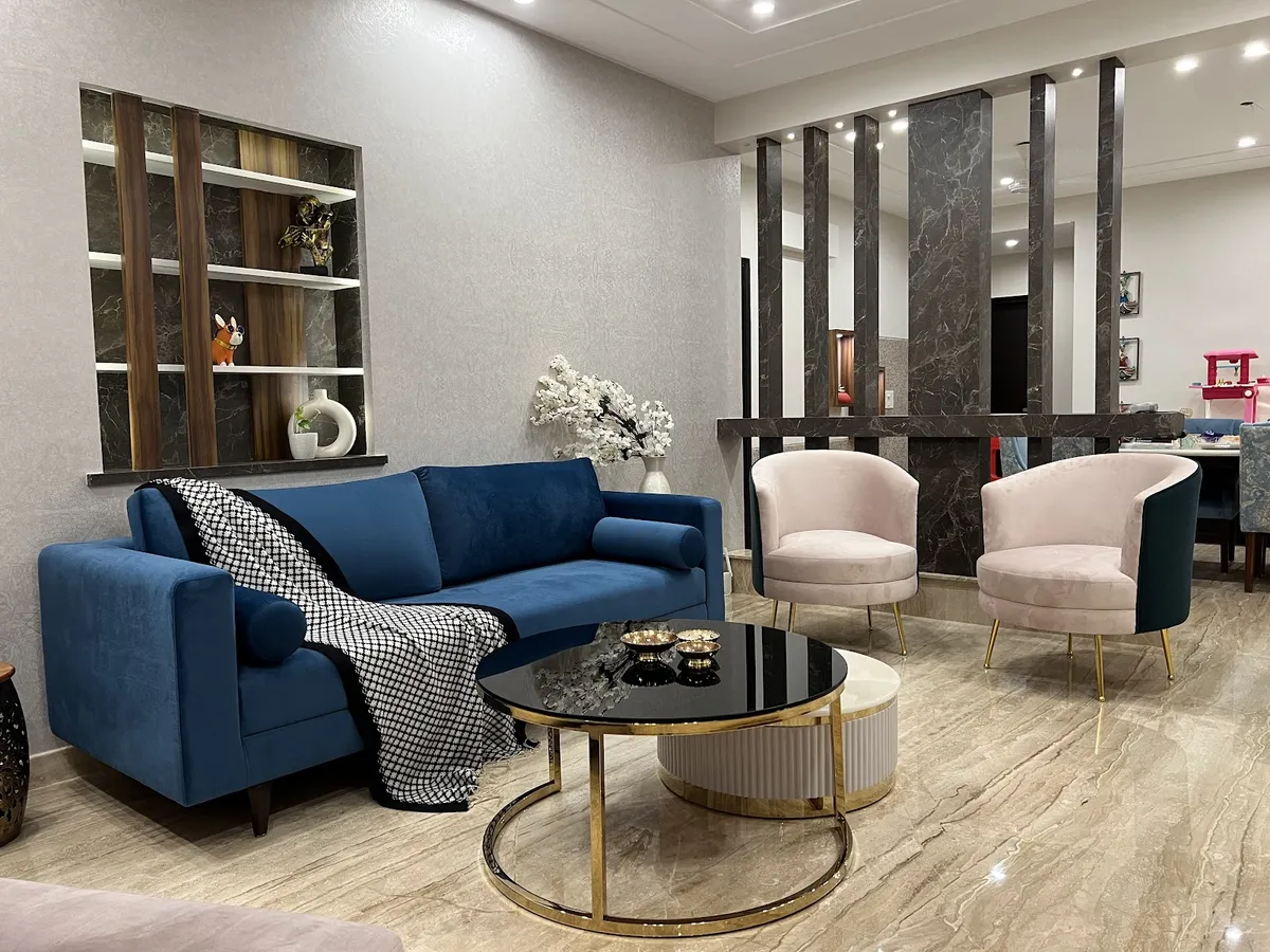 Sapphire velvet sofa and two blush tub chairs on gold legs face a dark-marble fin screen that separates the living zone from the dining