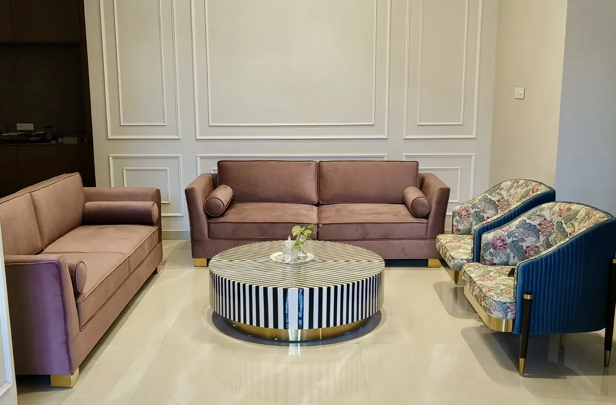 Two mauve velvet sofas on brass block feet facing each other across a round black-and-white striped inlay table with a brass base ring
