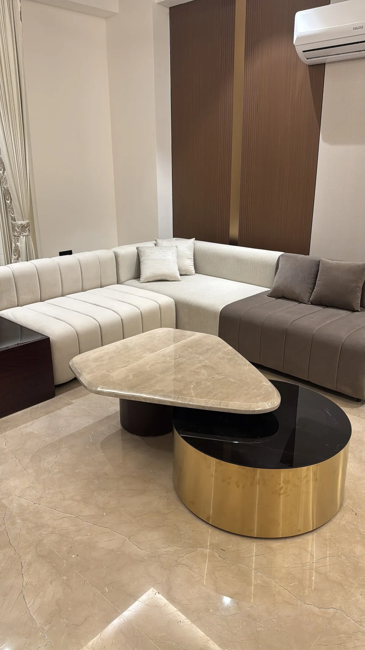 Ivory and mocha channel-tufted L-sectional against a fluted brown wood panel split by a brass reveal