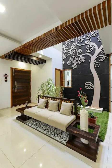 Entrance foyer with a low teak platform daybed over a pebble-filled recess, facing a double-height black stone wall carrying a white swirl-tree motif