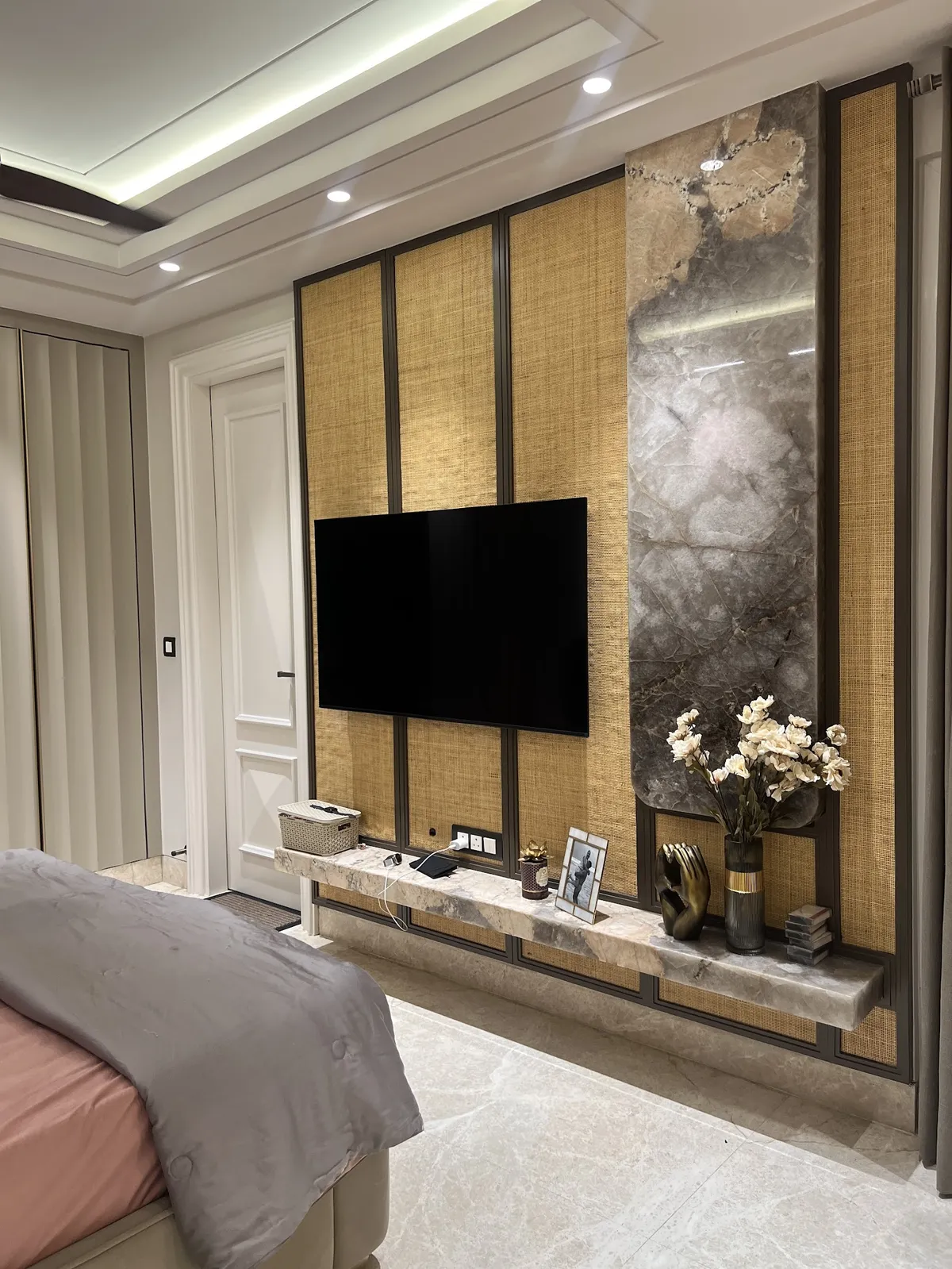 Bedroom TV wall of cane-webbing panels in slim black metal frames beside a grey marble slab strip