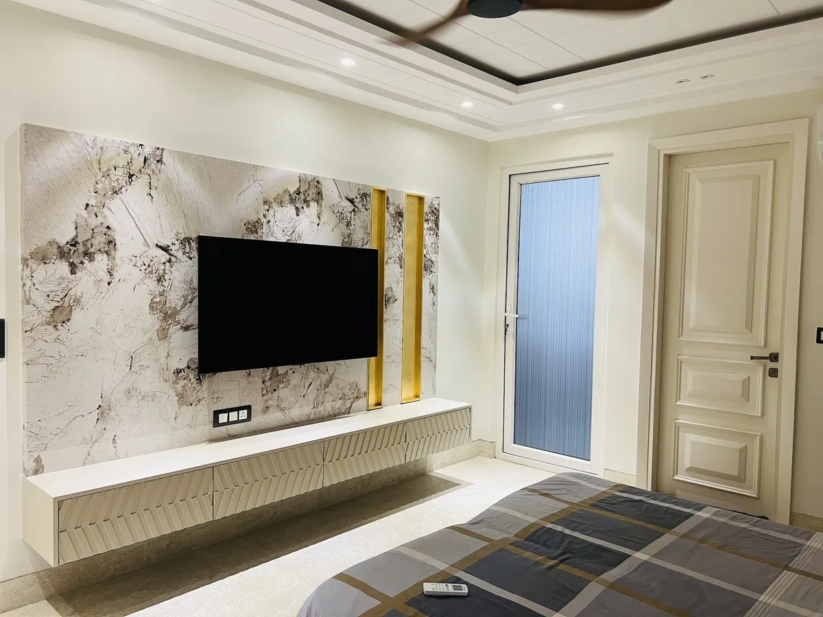 Master bedroom with a marble-panelled TV feature wall framed by gold accent strips, a floating fluted-front console