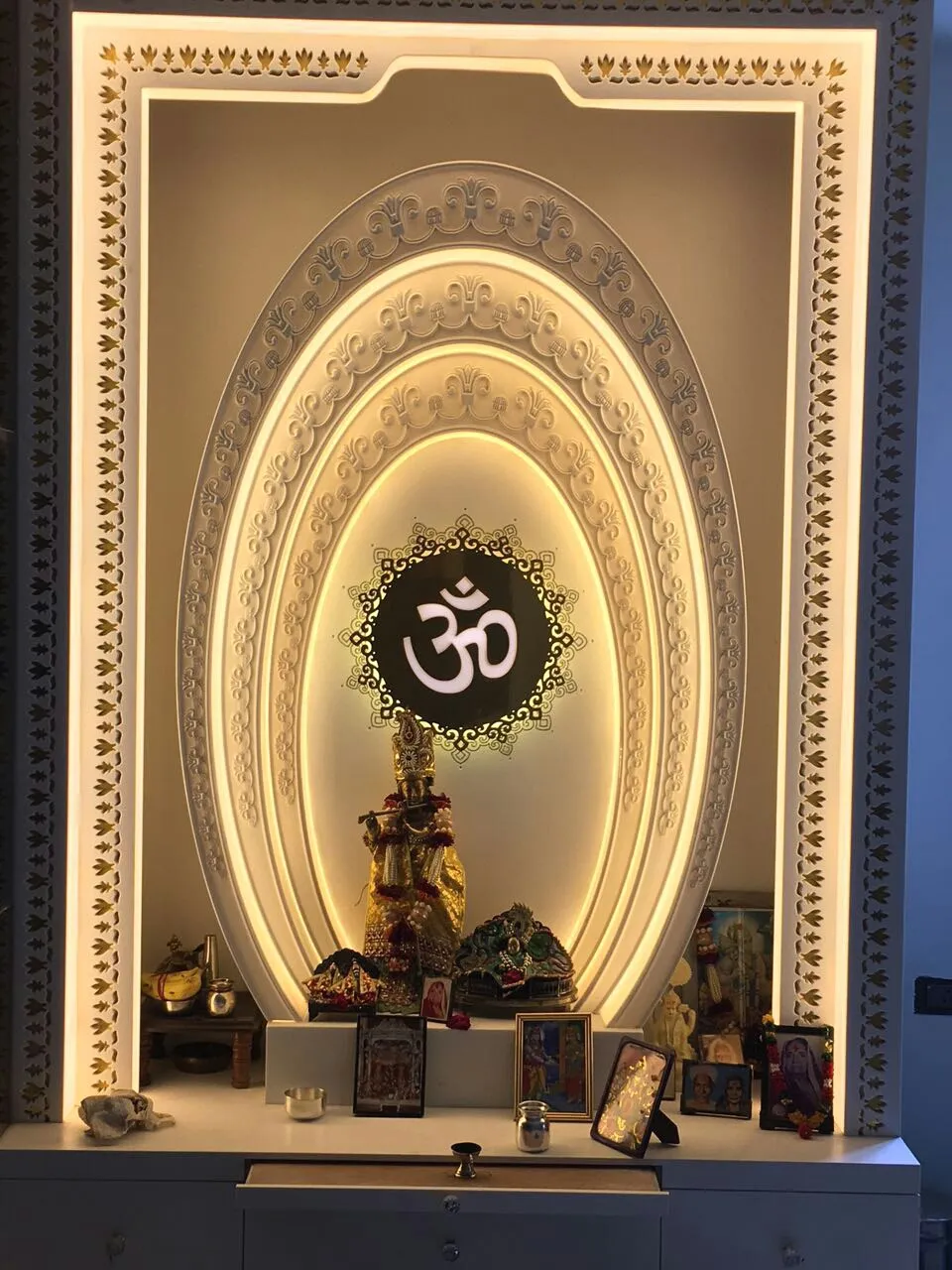 Home mandir built as concentric carved-ivory oval arches on concealed warm light, with a laser-cut gold leaf-motif border and a backlit Om medallion above a