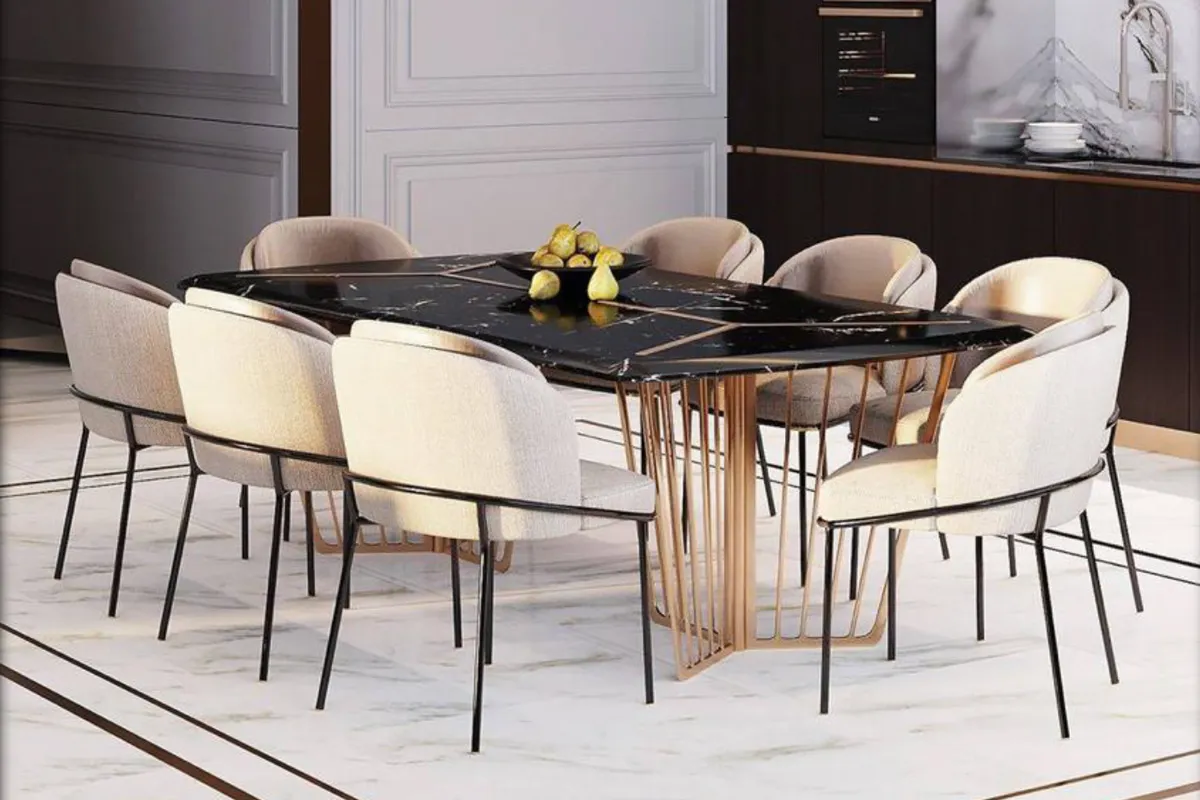 Render of a luxury dining room with a black marble table on a gold spoke pedestal base and cream upholstered chairs, opening into a dark wood modular kitchen.