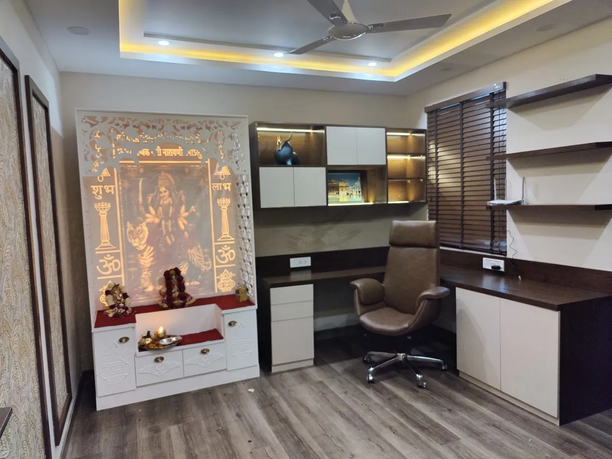 Home study where an L-shaped wenge desk run with white overhead cabinets shares the room with a backlit white mandir panel carved with Shubh-Labh