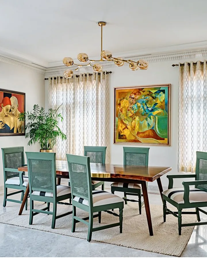 Dining room with a live-edge wood table, sage-green cane-back chairs, a branching gold pendant chandelier, and two large cubist paintings on the wall.