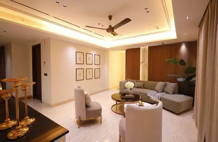 Living room with a cove-lit ceiling fan, cream armchairs with gold legs and a grey sectional sofa around round nesting coffee tables, a six-frame gallery wall