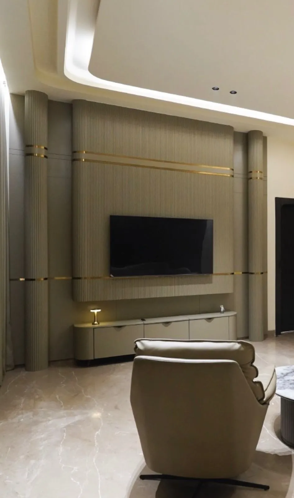 Render of a living room with a fluted taupe TV feature wall banded in gold trim, a curved cove ceiling, a rounded console