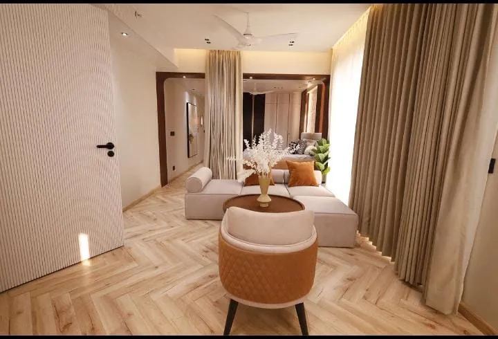 Render of a narrow beige living room — low modular sofa and a tan quilted tub chair around a round wood table on chevron-laid light wood flooring