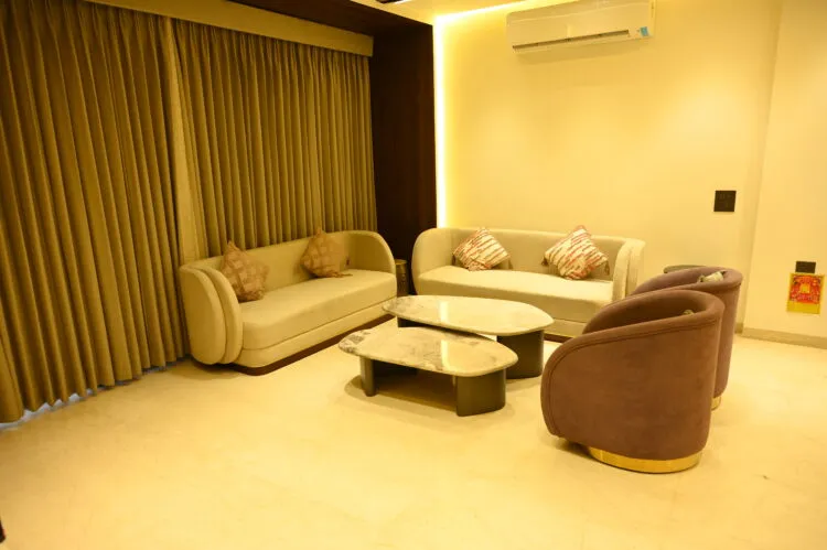 Photograph of a drawing room where two curved cream sofas face a pair of brown velvet swivel tub chairs on brass bases