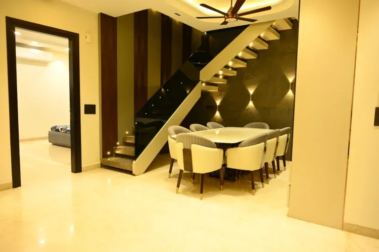 Dining area beneath a floating black-glass staircase, with a cream tufted dining chair set for eight