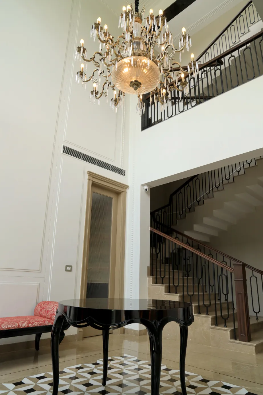 Double-height entrance hall with a brass and crystal chandelier over a black cabriole-leg centre table