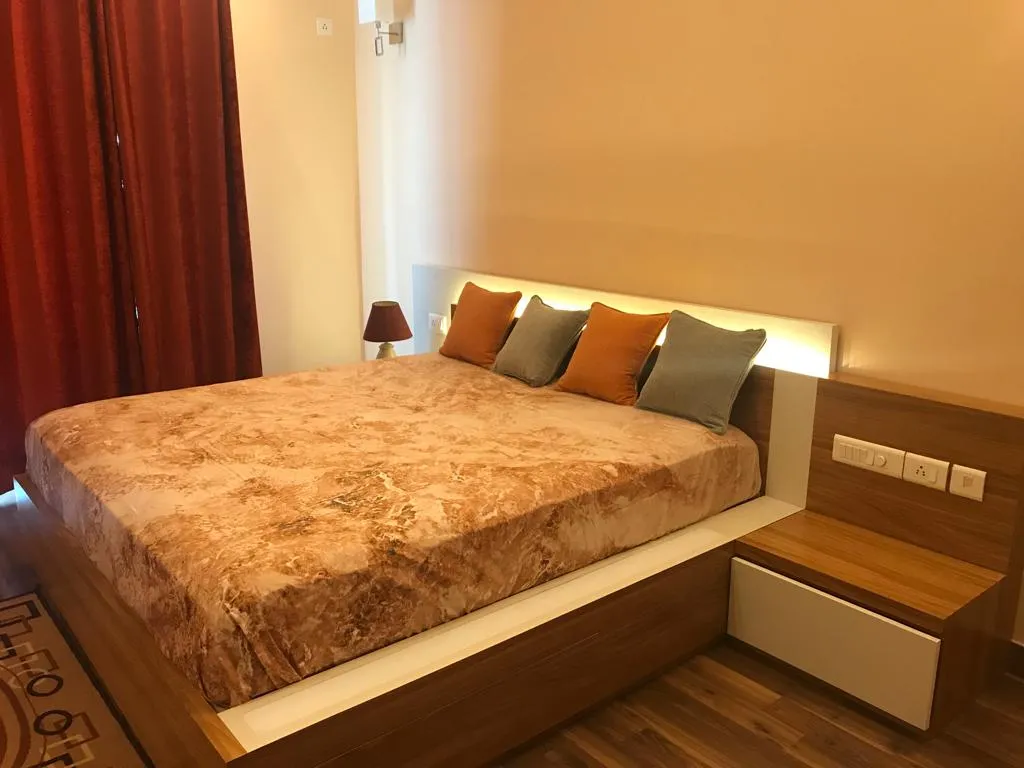 Bedroom with a wood-laminate platform bed lit from behind a white headboard band, a cantilevered bedside carrying the switch plate