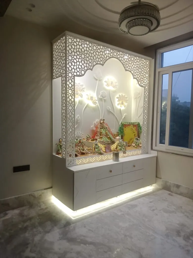 Freestanding white pooja mandir with CNC floral jaali sides, a carved lotus-relief backdrop lit from behind