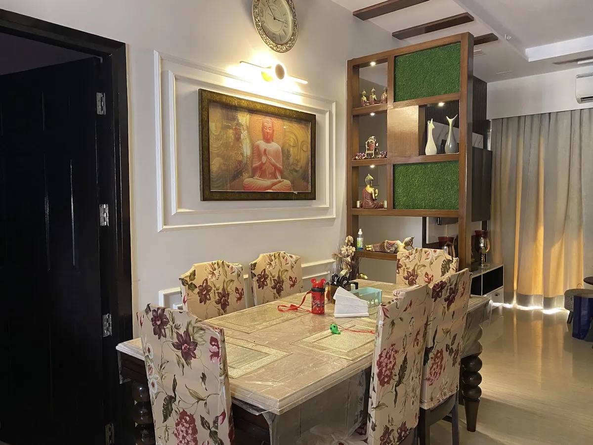Dining area with a marble-top table under floral slipcover chairs, a framed Buddha painting on a moulded wall panel