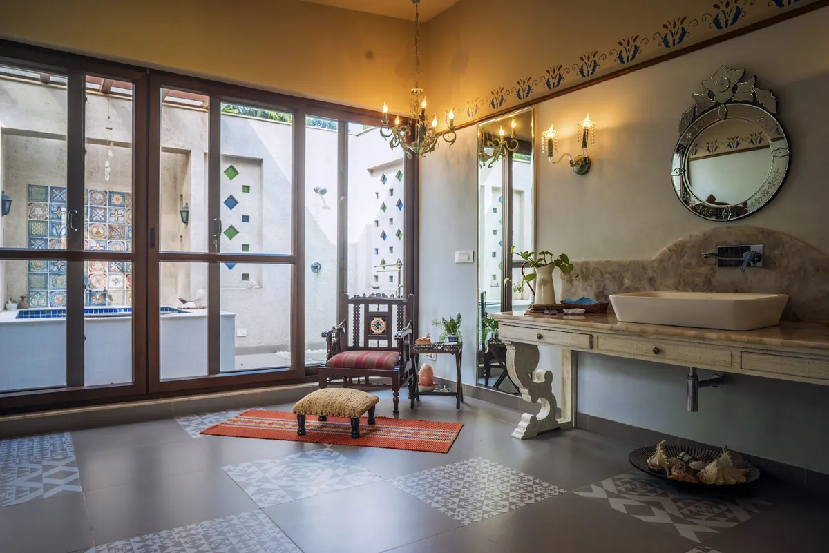Bathroom with a marble-topped wood console vanity, an ornate Venetian mirror and chandelier, glass doors opening onto an outdoor mosaic-tiled tub area.