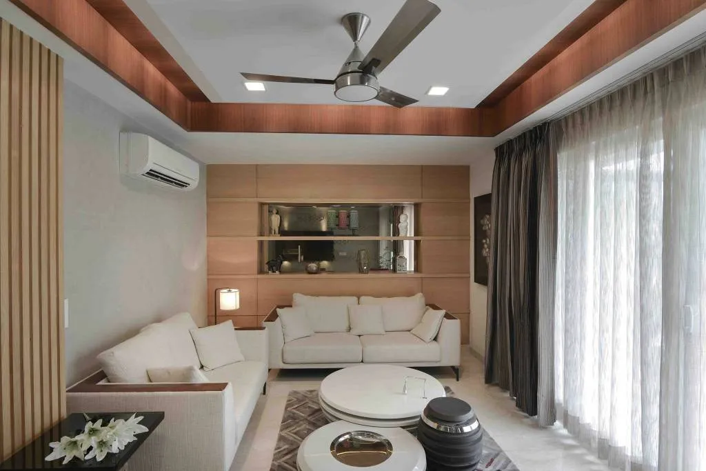 Living room with fluted wood wall panelling and a warm wood cove-lit ceiling, cream sofas around round nesting coffee tables and a built-in display shelf