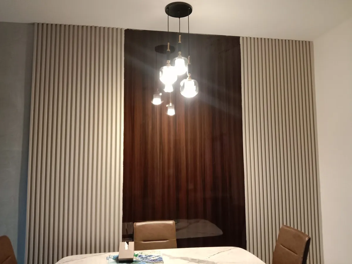 Dim dining corner where a faceted-glass cluster pendant drops over a marble-top table set against a dark walnut panel let into pale grey fluted walls.