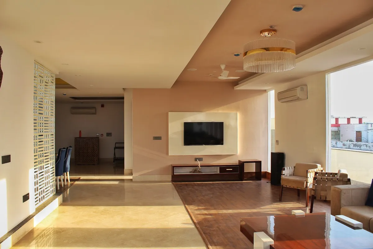 Wide living room where a dark timber-floored seating island with Jeanneret-style strap armchairs steps out of beige stone flooring