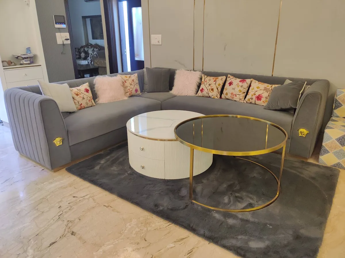Grey velvet corner sofa with gold medallion studs on its arms and a bank of floral and blush-fur cushions