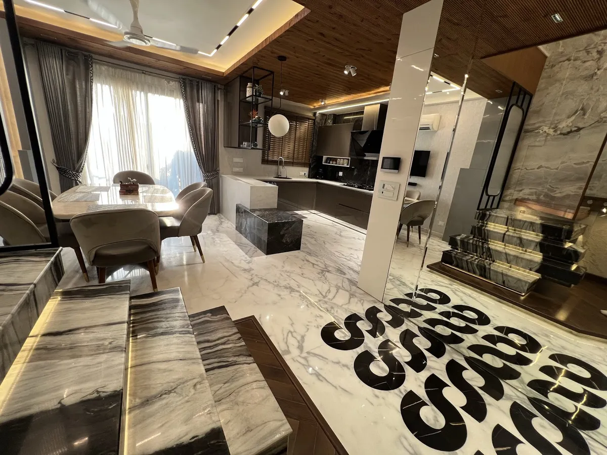 An open-plan dining-kitchen-foyer space with book-matched grey marble flooring featuring a bold graphic inlay pattern, a wood-slat ceiling