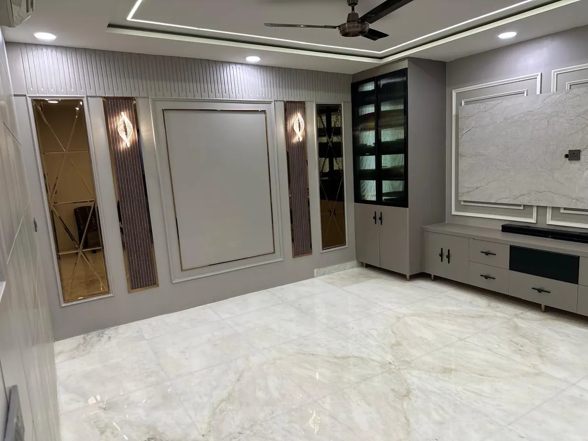 Unfurnished grey living room where fluted panels, bronze-tint bevelled mirror strips and a moulded blank frame face a marble-slab TV backdrop over a low