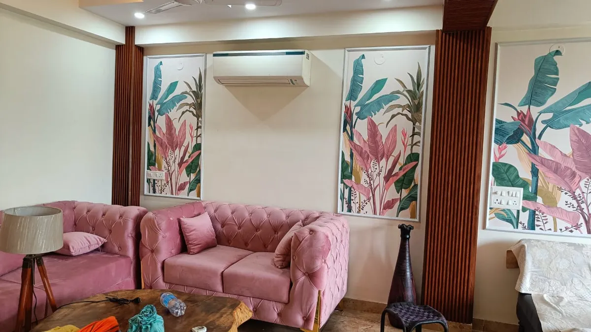A living room with a blush-pink tufted velvet sofa set against framed botanical wallpaper panels flanked by fluted wood pilasters.