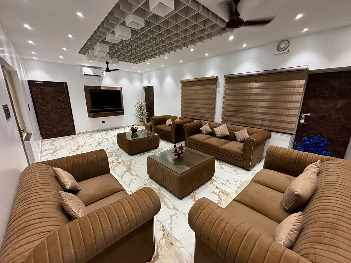 Big formal drawing room with four brown channel-tufted sofas ringing two matching upholstered coffee tables on gold-veined white marble