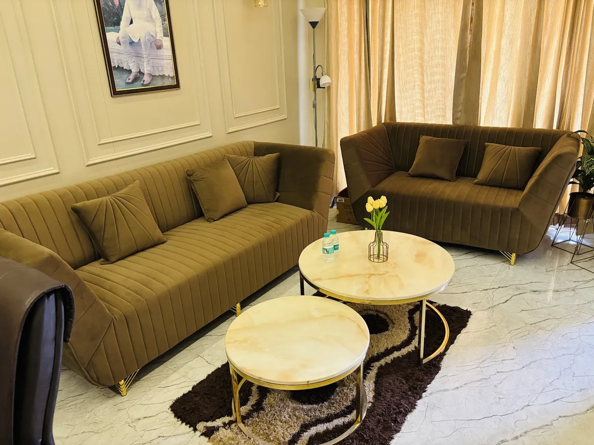 Living room with olive green channel-tufted velvet sofas, gold-framed marble nesting coffee tables and panel-moulded walls.