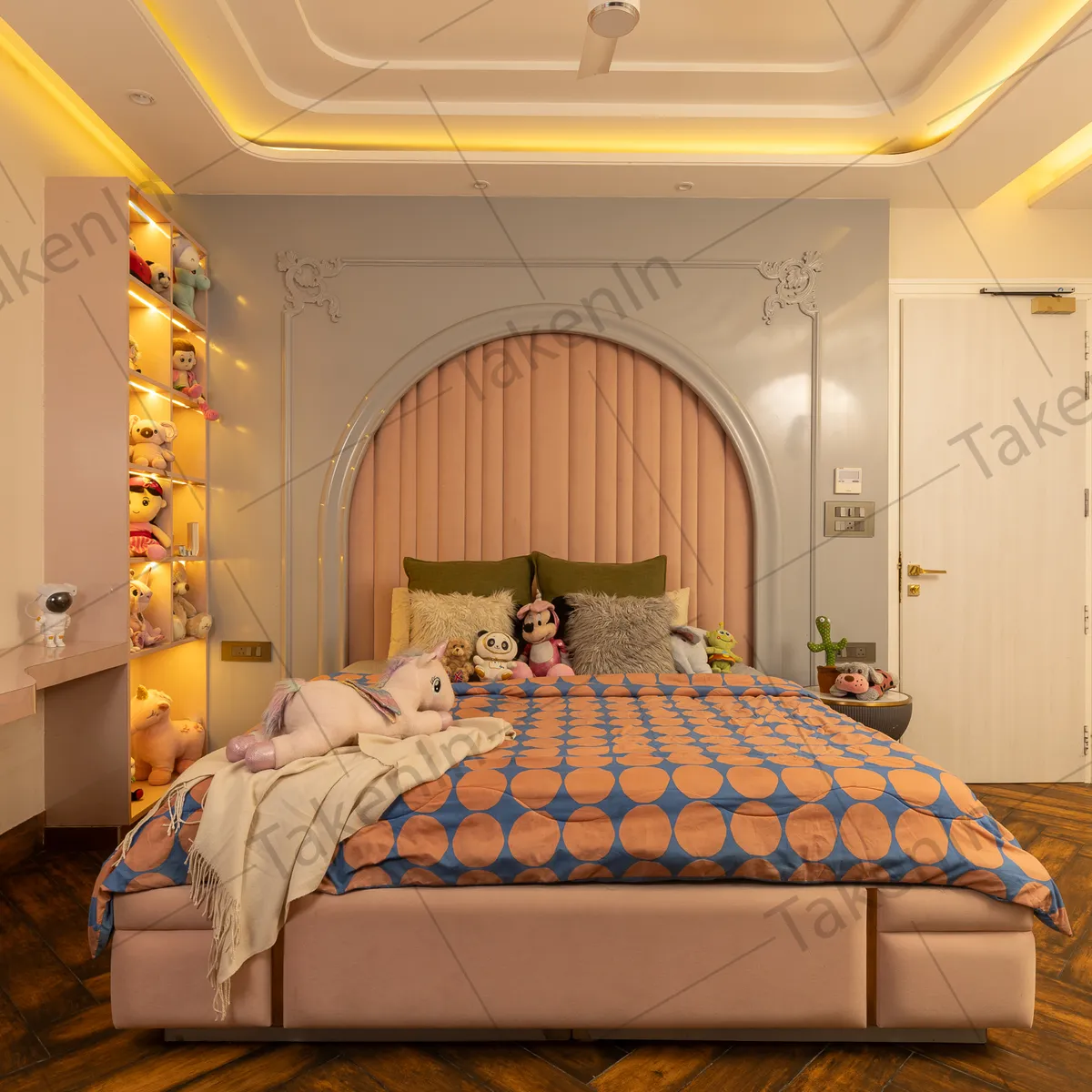 Kids' bedroom with a blush arched channel-tufted headboard set inside classical wall mouldings, a backlit column of niches packed with soft toys