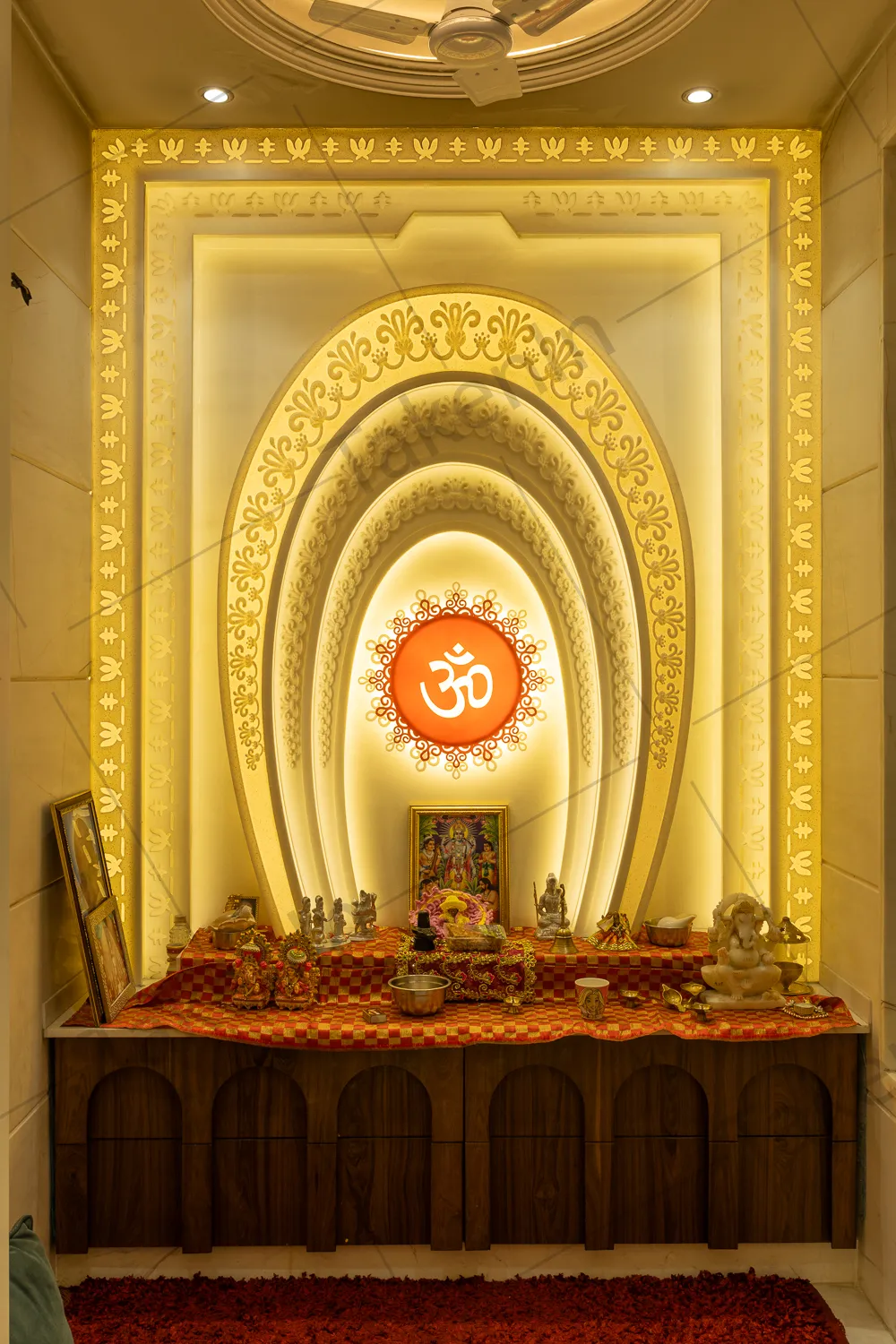 A backlit multi-tier arched pooja mandir with gold trim mouldings, an illuminated Om medallion