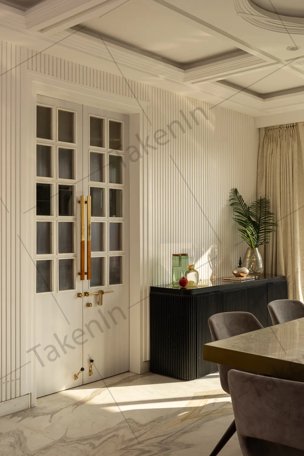 Dining room with a fluted glass-panel double door with gold handles, ribbed wall panelling, a black fluted sideboard styled with glass objects