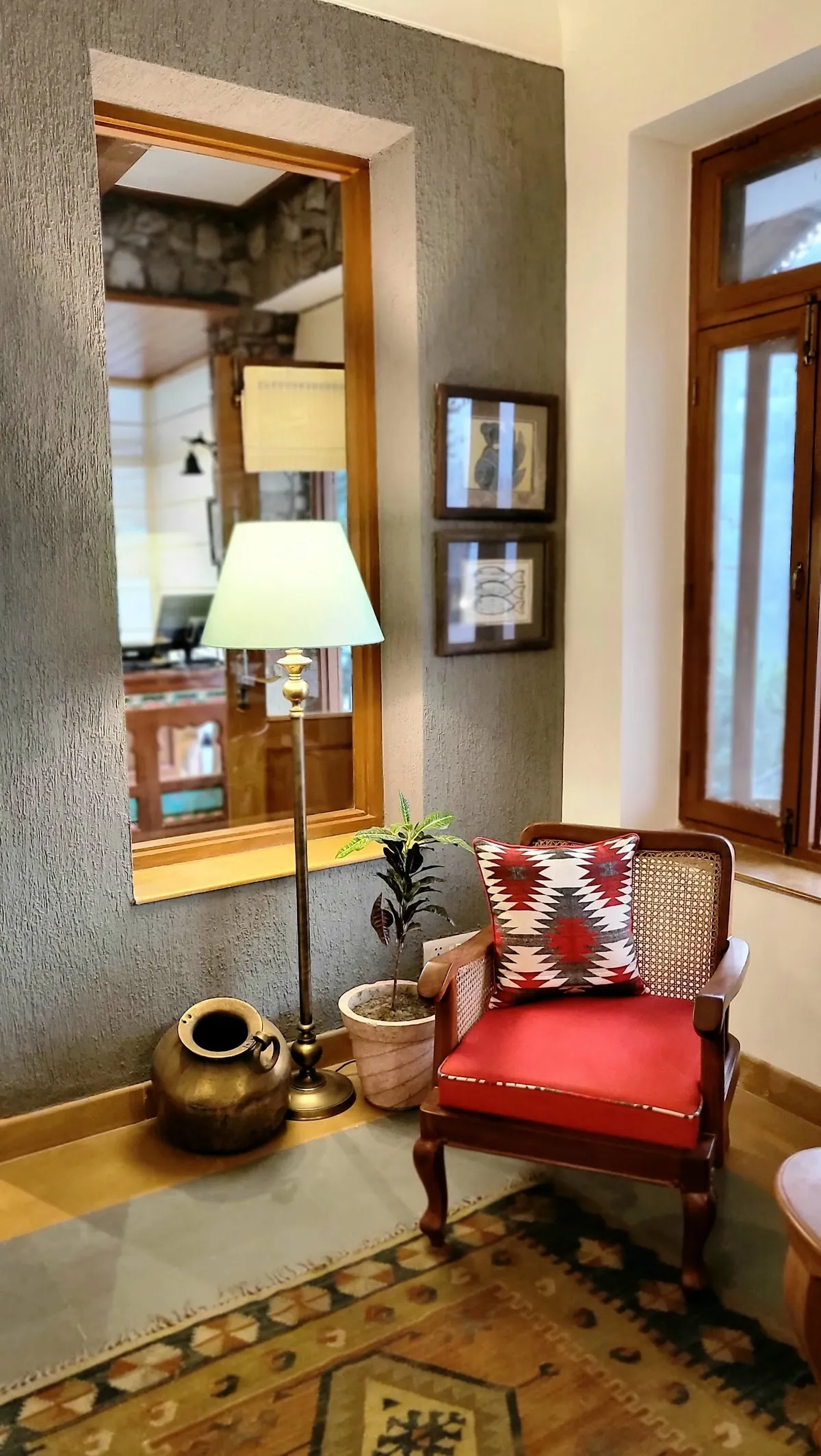 Sitting corner against a grey textured plaster wall — teak-framed mirror recessed above a ledge holding a brass pot and a brass floor lamp