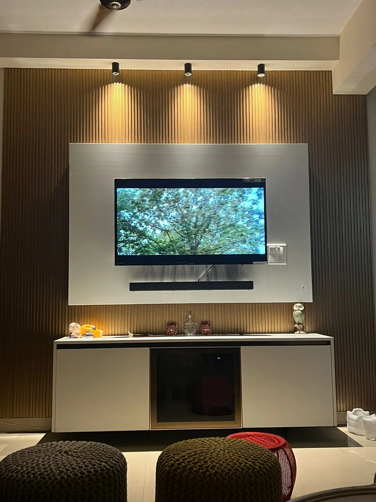 Living room TV wall with fluted wood panelling and a brushed-steel accent panel behind the screen, spotlighted from
