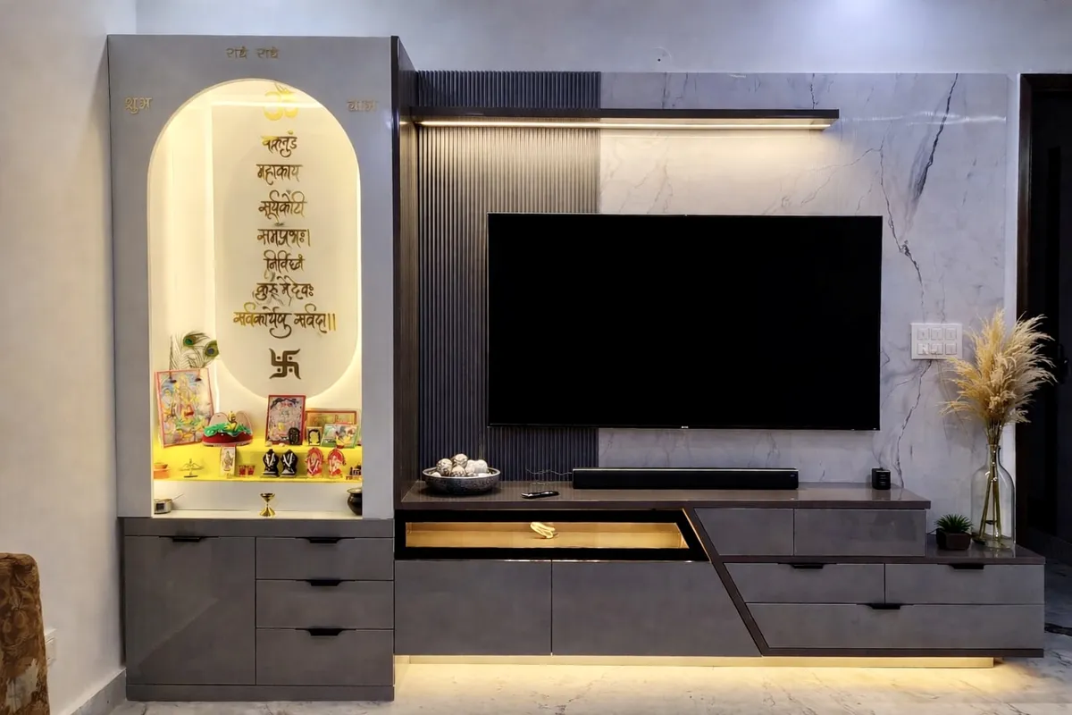 One wall carrying both a backlit arched pooja niche with a gold Sanskrit shloka on its back panel and a TV bay in grey veined marble with a dark fluted panel