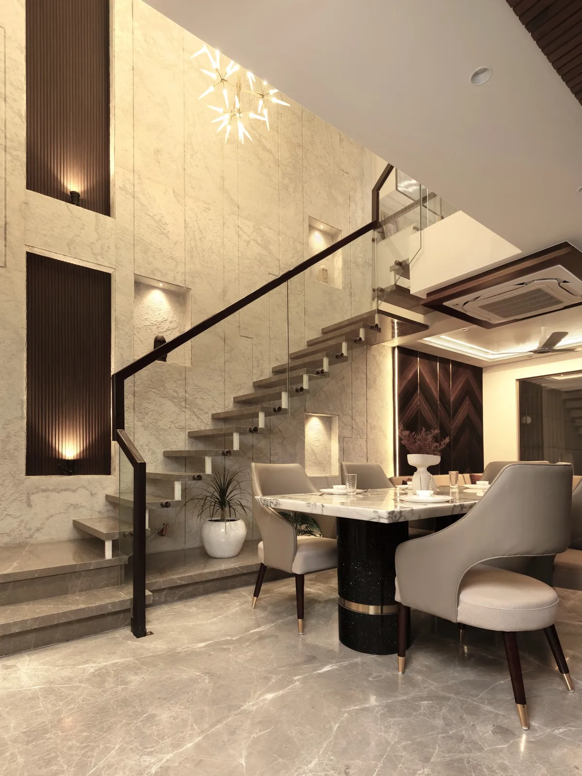 Dining nook beside a floating staircase, set against a book-matched marble slab wall with a starburst chandelier overhead.