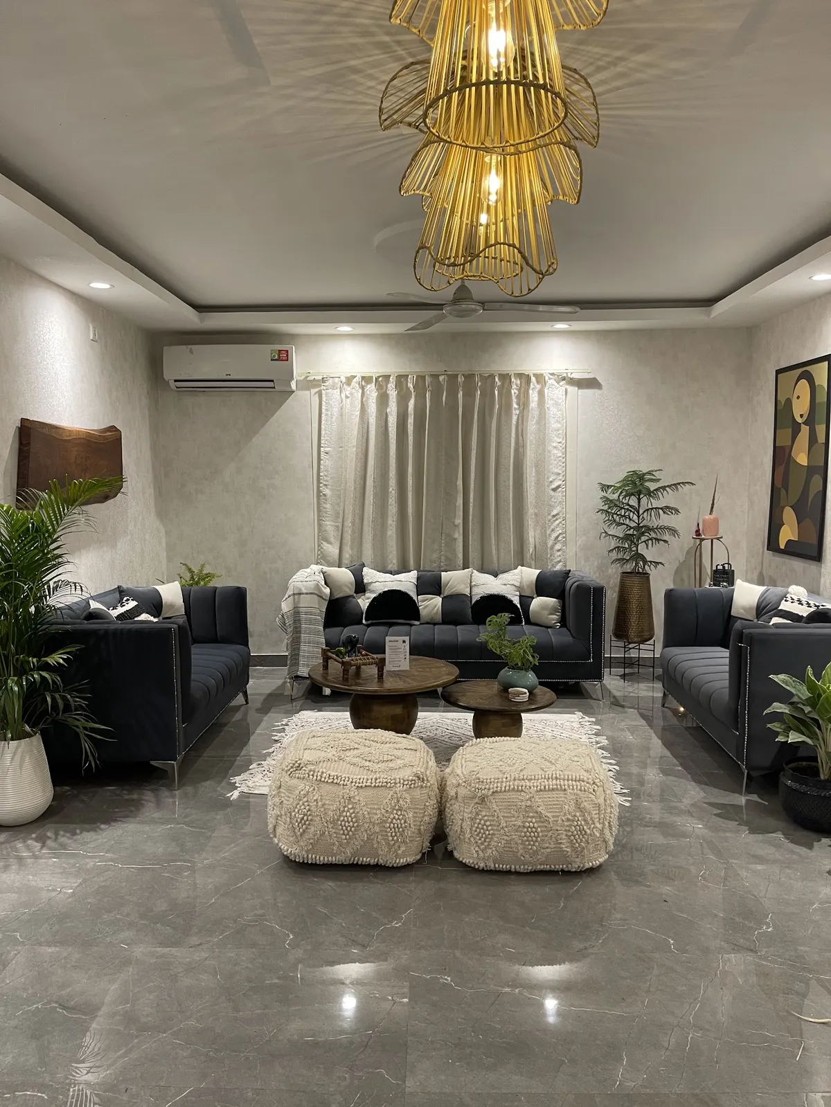 Night shot of a living room arranged symmetrically with three charcoal channel-tufted sofas around two round mango-wood tables
