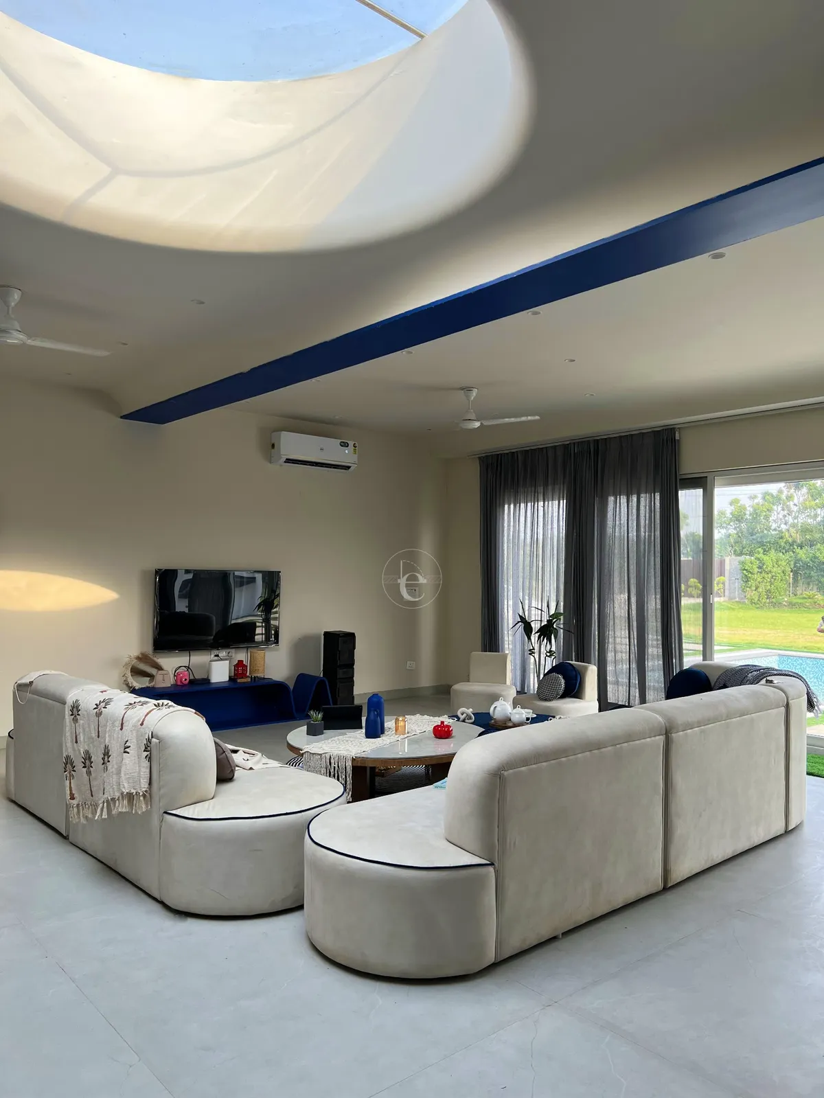 Two curved cream modular sofas facing each other under a sculpted ceiling with a circular skylight and a painted cobalt band