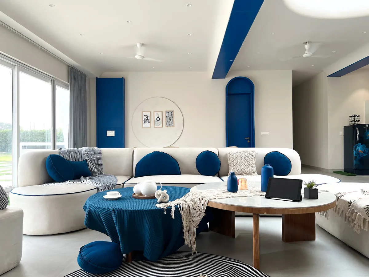 Living room with a curved white sofa dressed in cobalt blue round cushions, an arched blue-painted internal door