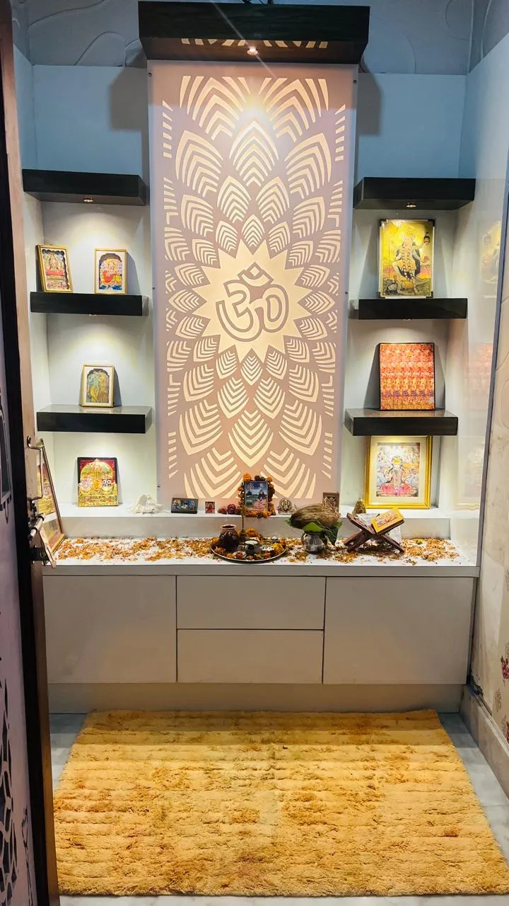 A backlit CNC-cut Om jaali panel forms the focal wall of this pooja unit, flanked by floating shelves for framed deities above a closed storage counter.