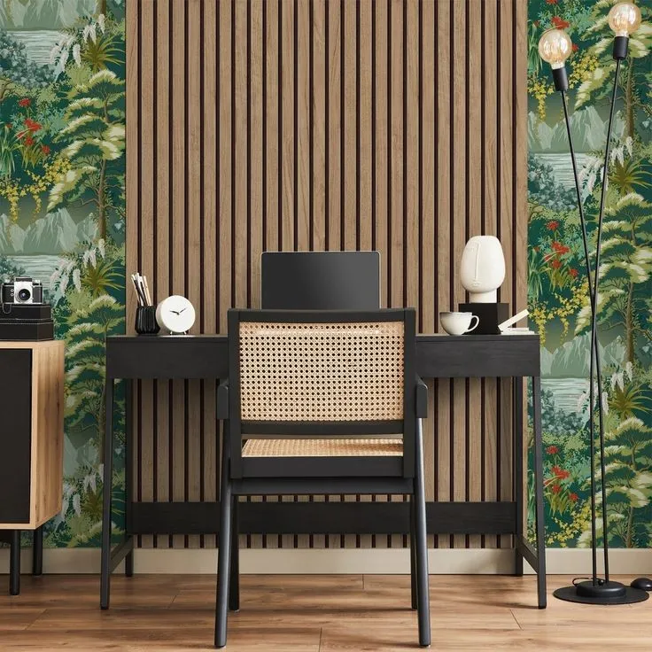 Black writing desk and caned Jeanneret-style armchair centred on a walnut acoustic slat panel, flanked by tropical green foliage wallpaper