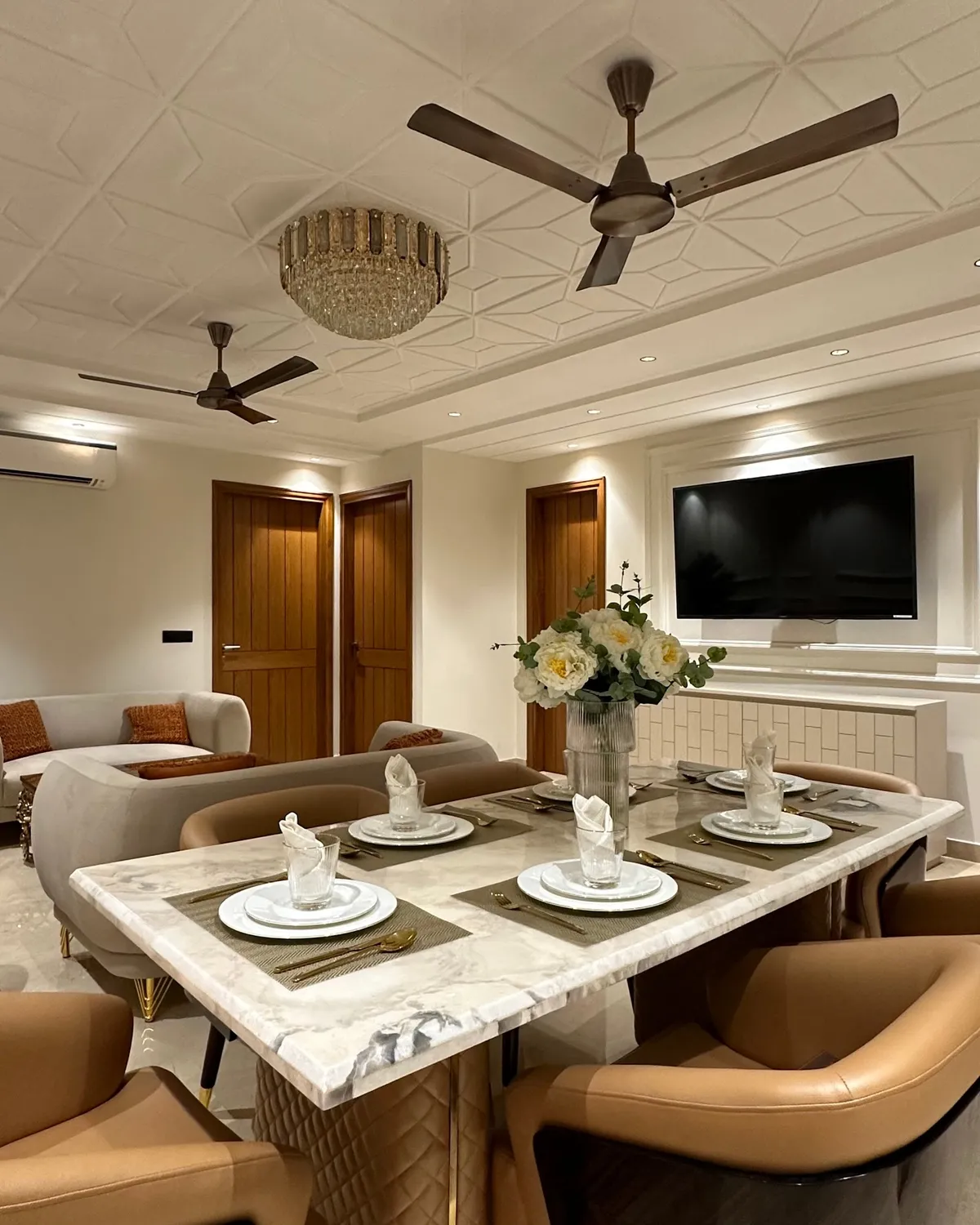 Marble-topped six-seater laid with jute placemats and folded napkins under a crystal drum chandelier, tan leather chairs around it