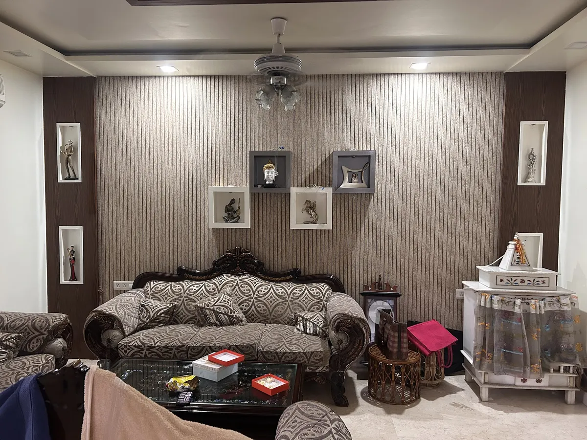 Living room with a striped wallpaper feature wall, framed curio niches displaying figurines, a carved wood-frame upholstered sofa