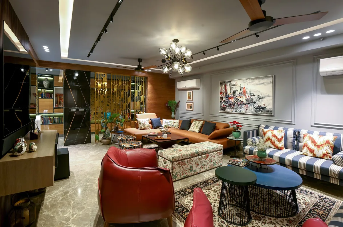 Long eclectic living room where a brass geometric jaali screen separates a lit book niche from a tan leather sectional, facing a striped blue settee
