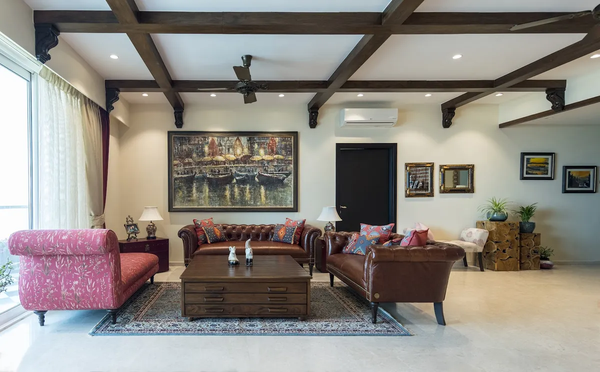 Living room with an exposed dark wood beam-and-corbel ceiling, tufted brown leather chesterfield sofas, a pink floral chaise